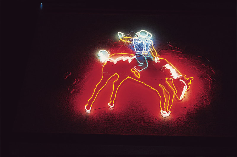 A neon sign that shows a blue and gold neon cowboy on a red bucking bronco, illuminated at night
