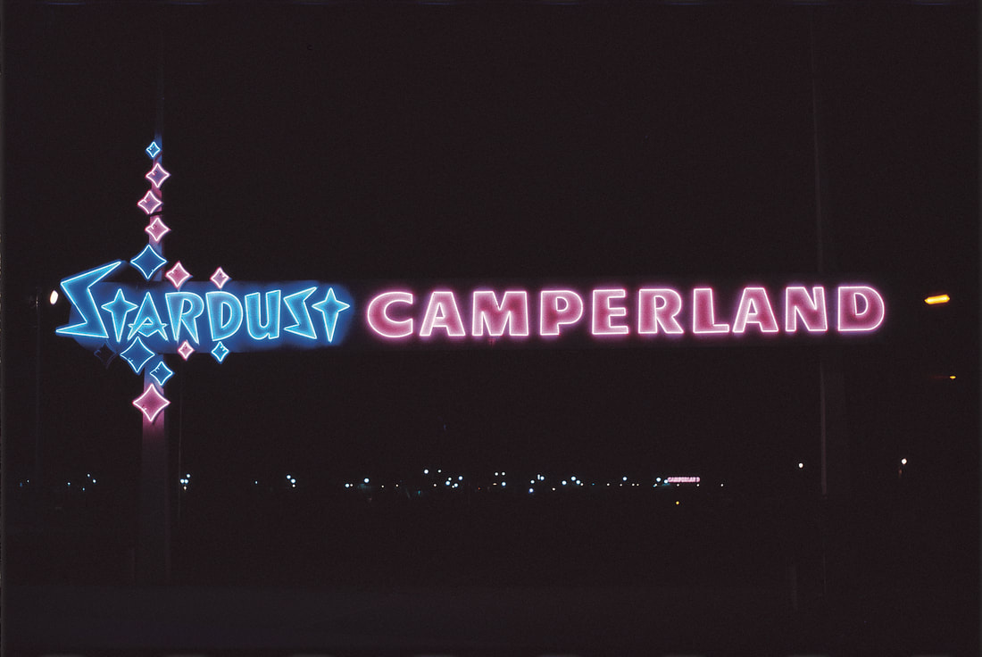 A neon sign that says Stardust in blue neon and Camperland in purple neon. It is nighttime and the signs are illuminated.